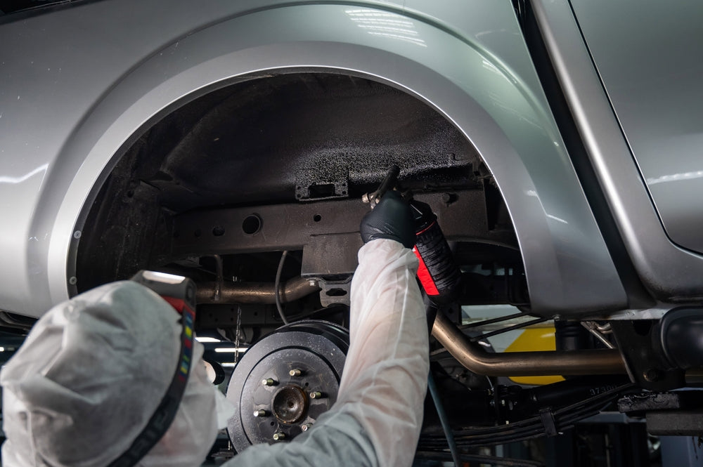 Werkstatttechniker sprüht Unterbodenschutz in einen Autoradkasten